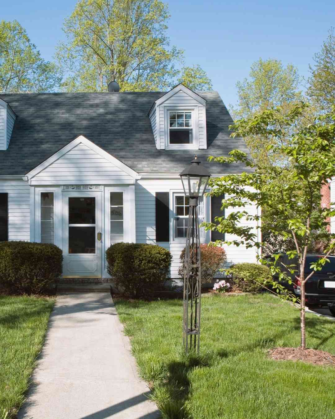 White house with black roof, front yard, and trees in spring.
